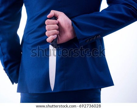 Young businessman holding knife on the back isolated from a white background.