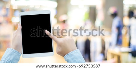 Hand using tablet with blank screen for mock up over blur store background, banner, business and technology concept, digital marketing, seo, e-commerce