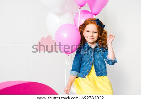 beautiful little redhead girl sitting with balloons and smiling at camera at birthday party