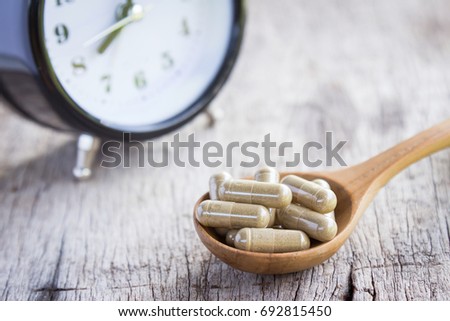 Herbal capsules with alarm clock for eating time on rustic wooden table, healthy living with natural remedy 