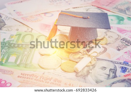 International graduate study abroad program concept : Black graduation cap on pile of foreign currency or money from EU euro, US dollar, Japan yen, China and a scroll of diploma or certificate nearby.