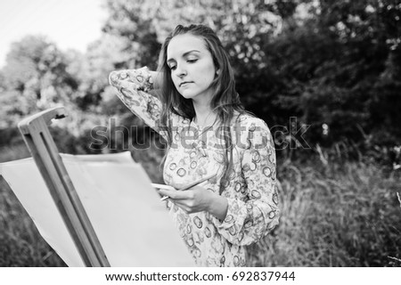 Portrait of an attractive young woman in long dress painting with watercolor in nature. Black and white photo.