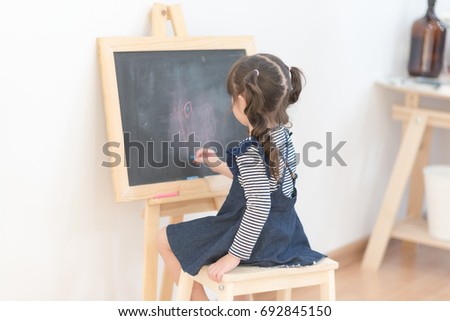Happy asian girl kid draw cartoon with chalk on blackboard for learning at home. Photo for kid education and school study concept.