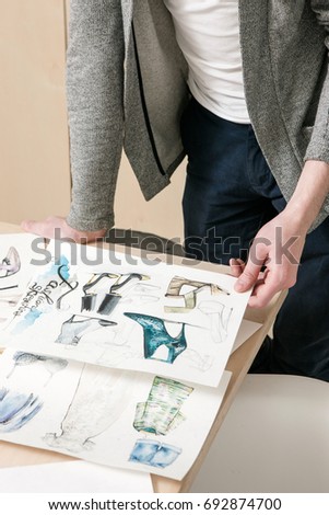 Designer work on fashion sketches. Unrecognizable man with pictures of clothes and footwear in hands. New collection, vogue project, creative artist exam concept