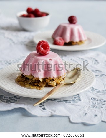 Homemade raspberry cheesecake ice cream with fresh berries and oatmeal, served on a plate on lace napkin. Light grey stone background.