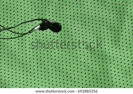 Black earphones lie on the green sportswear of polyester nylon fiber. The concept of listening to music during sports training with modern technology