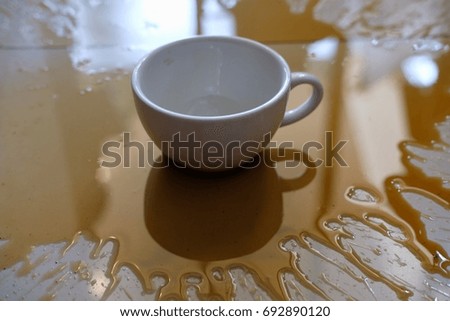 Coffee spilled from the white cup on the white floor.