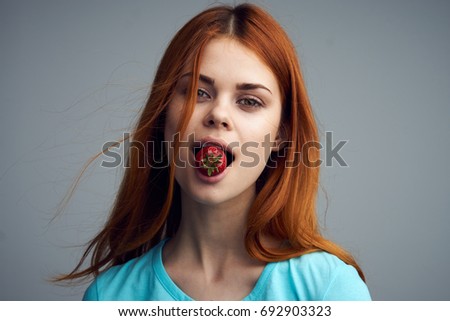 A woman in her mouth a strawberry on a gray background, a berry portrait                               