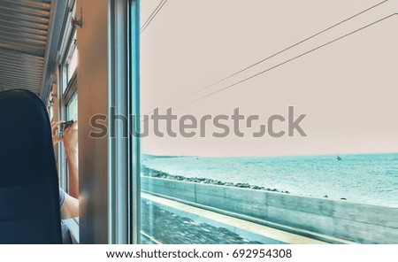 Woman taking photos from her seat while train moves near the sea