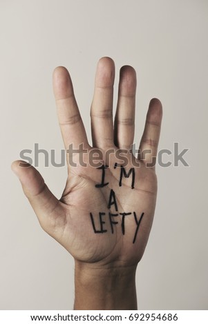 the text I am a lefty written in the palm of a left-handed man, against a beige background Royalty-Free Stock Photo #692954686