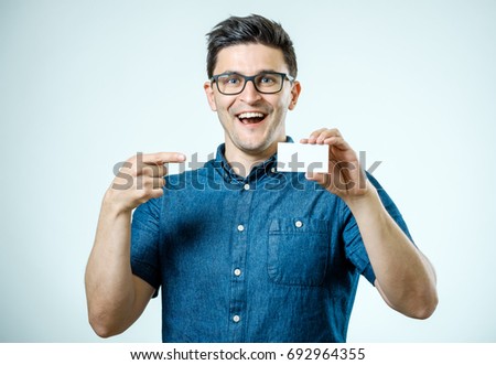 Young man showing blank business card or sign. Isolated on gray
