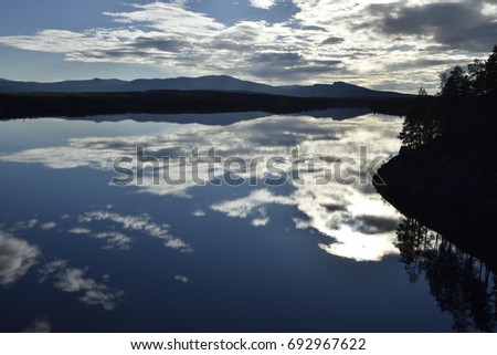Calm lake with reflections from the sky, blue sky with some clouds  and mountains in background, picture from the Northern Sweden.