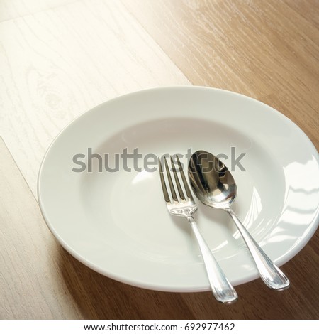 Spoon and fork on white plate, on wooden floor.