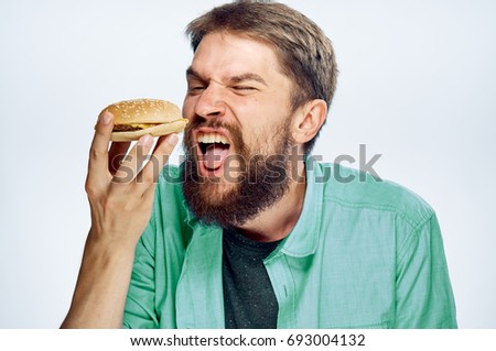 Man with a beard holding a hamburger on a white isolated background, emotions, portrait.