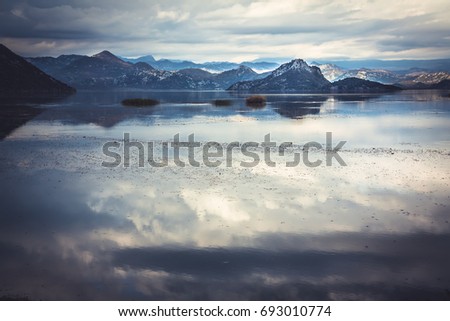 Tranquil water with sky reflection and mountains  landscape in overcast day with dramatic sky in Europe country Montenegro at Skadar lake