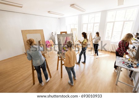 creativity, education and people concept - group of woman artists or students with brushes and palettes painting and drawing still life picture on easels at art school studio Royalty-Free Stock Photo #693010933