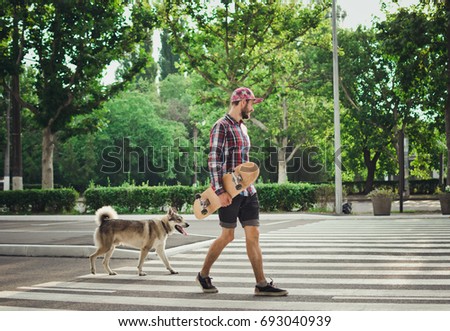 Young man walking with skateboard and siberian husky dog on street road