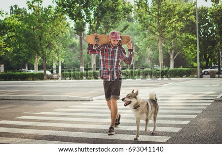 Young hipster man walking with skateboard and siberian husky dog on street road