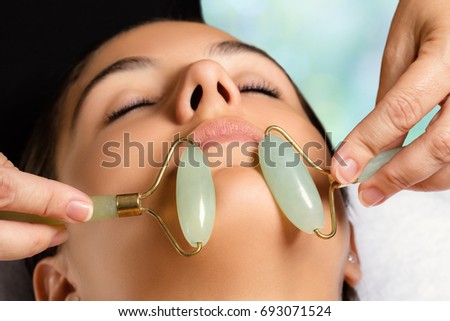 Macro close up portrait of woman having facial beauty treatment in spa. Therapist massaging chin with jade rollers.
 Royalty-Free Stock Photo #693071524