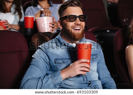 Photo of concentrated young man sitting in cinema watch film drinking aerated sweet water.