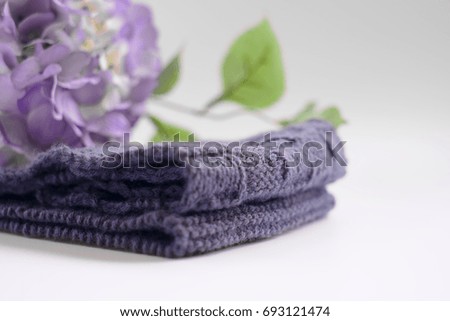 Selective focus image of a grey handmade scarf on a white floor with blurred purple flower background.