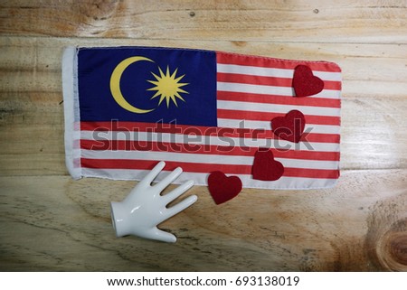A Malaysian flag, hearts shape and a hand : symbol of unity on a wooden background. Concept for 60th year of Malaysian Independence Day.