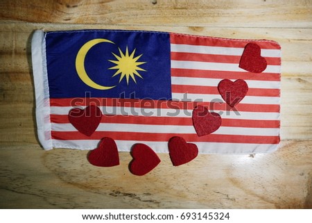 A Malaysian flag and a red hearts shape on a wooden background.  Concept for 60th year of Malaysian Independence Day.