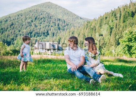 parents play with daughter on the field with mountains with forest on background
