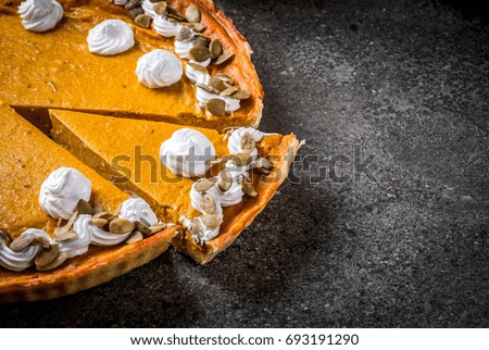 Traditional autumn dishes. Halloween, Thanksgiving. Sliced spicy pumpkin pie with whipped cream & pumpkin seeds on black stone table. Copy space
