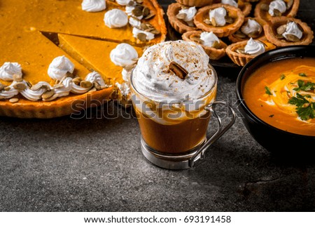 Set of traditional autumn food. Halloween, Thanksgiving. Spicy pumpkin latte, pumpkin pie and tartalets with whipped cream and pumpkin seeds, pumpkin soup, on black stone table. Copy space