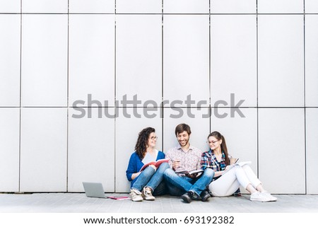 Young people are using different gadgets and smiling, sitting near the wall. Students studying using laptop computer. Education social media concept.