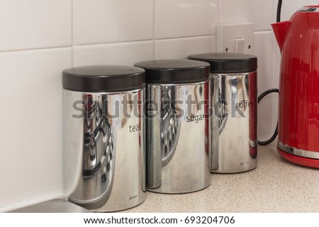 shiny silver coffee, tea and sugar storage jars and red kettle on a kitchen work top.
