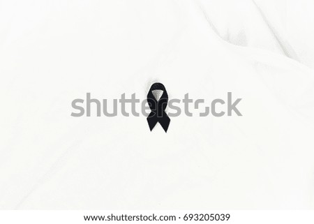 Black awareness ribbon on white fabric, for background.