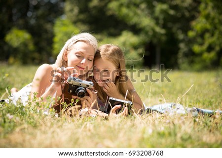 Mother teaching daughter how to take pictures on camera. Happy moments together, mom and child girl taking pictures.