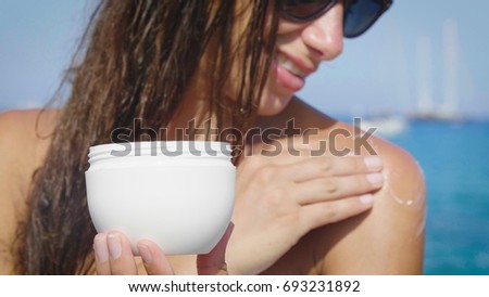Beautiful girl rinsing the body of a cramping cream, on the sea, in a white bikini smiling, sunglasses, background of sea blue water. Concept: beauty, vacation, spa procedures, spa bio cream, summer.