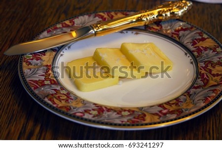 Three slices of butter with a golden knife in a round white plate with printed border