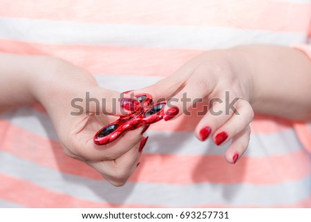 A girl is holding a popular toy metallic red fidget spinner in her hands. Stress relief. Anti stress and relaxation fidgets, spinner for tired people. Girl playing with a fidget spinner.
