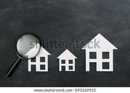 paper house model presenting on black chalkboard with magnifier tool showing estate investment concept. high angle view photo.