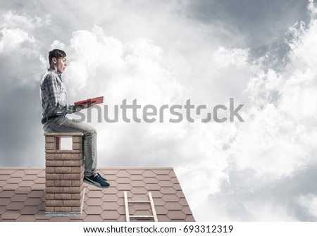 Young man in casual sitting on house chimney with red book in hands