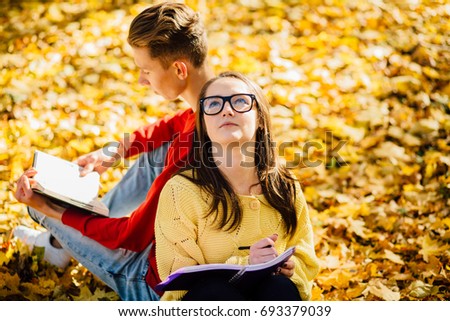 Series photo of beautiful young brunette woman in sunglasses and young man in red shirt sitting back to back on a fallen autumn leaves in a park and reading a book