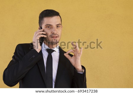 Man in suit making ok sign and talking with cellphone