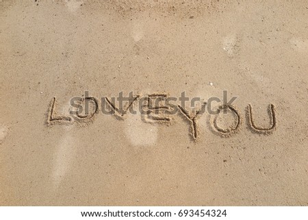 Handwriting  words "LOVE YOU" on sand of beach.