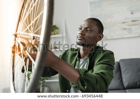 close-up view of pensive afro man checking bicycle wheel at home