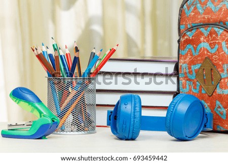 School backpack with school supplies. Books, metal stand for pencils with color pencils, stapler and headphones on wooden table. Back to school concept.