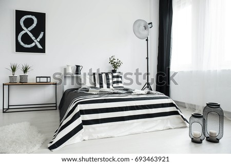 Two lanterns with candles on floor in front of king-size bed in bedroom with black poster on white wall