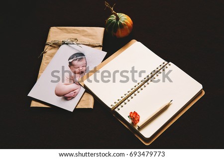 Printed card with sleeping newborn baby on knitted background with envelope, and an empty paper notepad for notes. Autumn baby background with autumnal attributes. Concept of message.