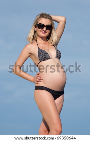 Pregnant woman in swimwear outdoors. Attractive expectant mother in bikini looks through sunglasses at camera