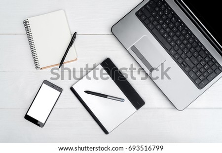 Top view on white wooden table with open blank laptop computer, cell phone, empty diary and graphic tablet, free space. Mobile phone with white screen, copy space 