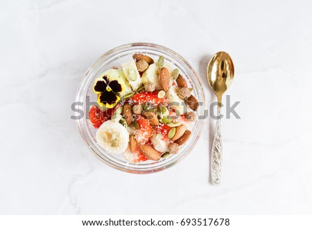 Healthy breakfast with yoghurt, strawberries, bananas, nuts, seeds and pansy flower. Vegan breakfast. Plantbased diet. Marble background.