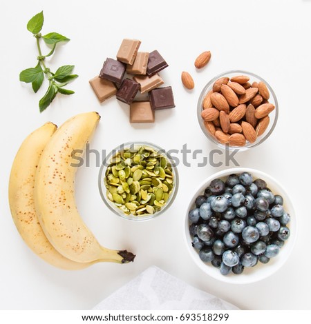 Healthy snacks: bananas, pumpkin seeds, vegan raw chocolate, almonds, blueberries and mint leaves. Vegan lifestyle. Natural sweets. Healthy diet. Top view Royalty-Free Stock Photo #693518299